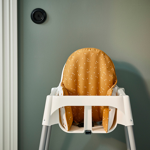 Una silla alta blanca con un cojín de puntos amarillos proporciona un apoyo seguro y cómodo para los niños pequeños durante la hora de comer.