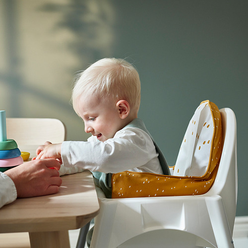 Bebé en silla alta con cojín de soporte inflable, jugando con bloques de colores sobre una mesa.