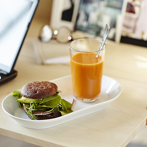 Una comida con un sándwich relleno de verduras y un vaso de jugo de naranja en un plato blanco.