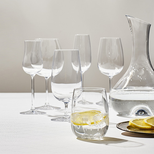 Cristalería STORSINT con diferentes formas y tamaños para diferentes bebidas, una jarra y rodajas de limón, dispuestas sobre un mantel blanco.