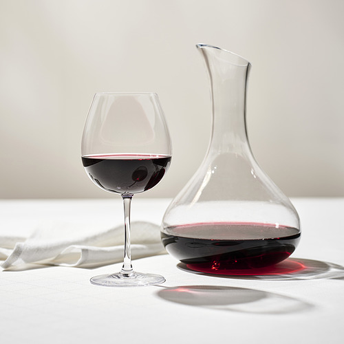 Decantador de vino transparente y vaso sobre mantel blanco, relleno de vino tinto para degustación.