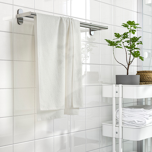 Toalla ludvial blanca sobre perchero de acero en un baño con azulejos y estanterías blancas.