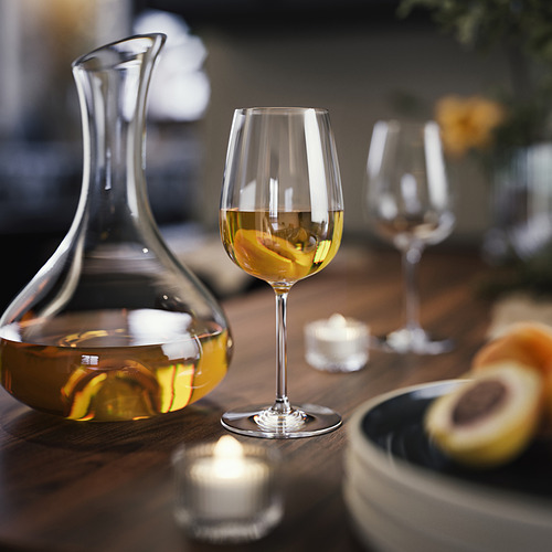 Mesa con cristalería transparente, que incluye una jarra, copas de vino y un vaso vacío. Diseñado para vino blanco, con velas y comida.