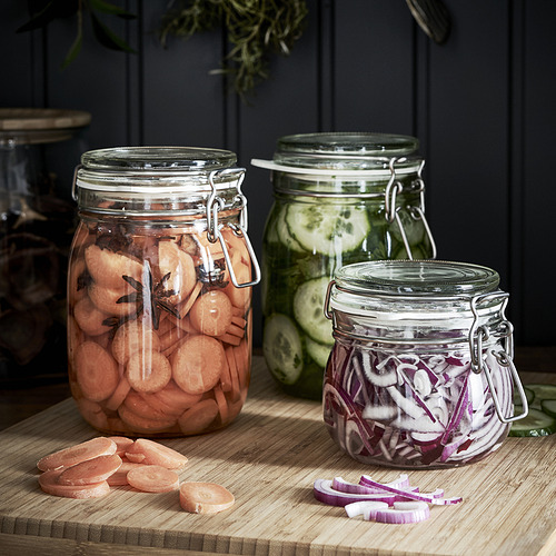 Tarros de metal con verduras en escabeche sobre tabla de madera, serie KORKEN.
