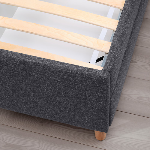 Cama tapizada en color gris oscuro con listones y patas de madera, con cajones de almacenaje.