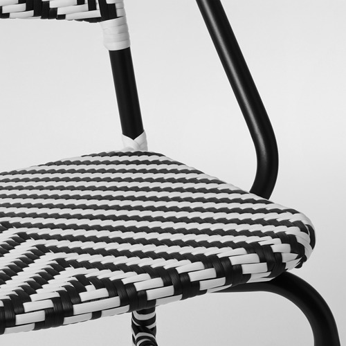 Silla tejida en blanco y negro con estructura de metal curvada, meticulosamente elaborada, que muestra un diseño de alta calidad y durabilidad.