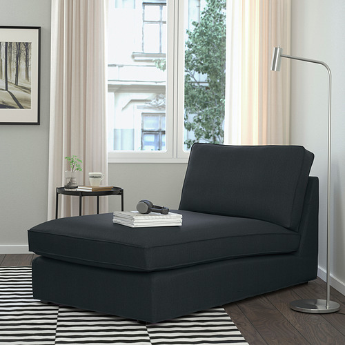 Moderna chaise longue KIVIK gris junto a la ventana, con lámpara y mesa auxiliar. Diseño cómodo y sencillo.
