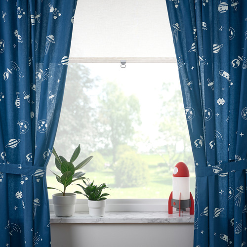 Las cortinas azules enmarcan una ventana con plantas y una lámpara cohete, que muestra vistas verdes al exterior.