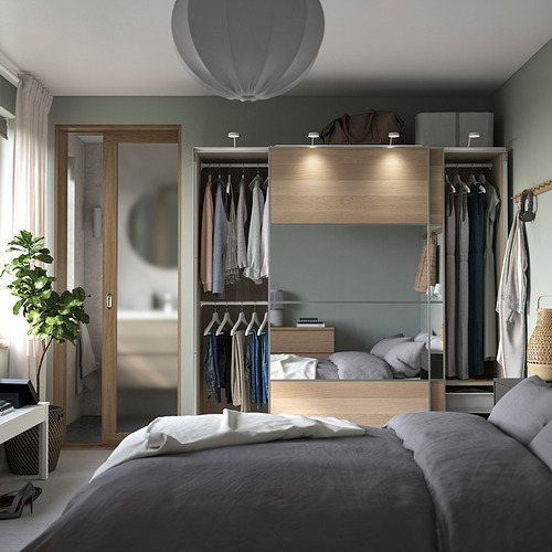 Dormitorio moderno con armario PAX, puertas corredizas, ropa organizada, iluminación integrada, sábanas grises, almohadas blancas, detalles en madera y paredes verdes.