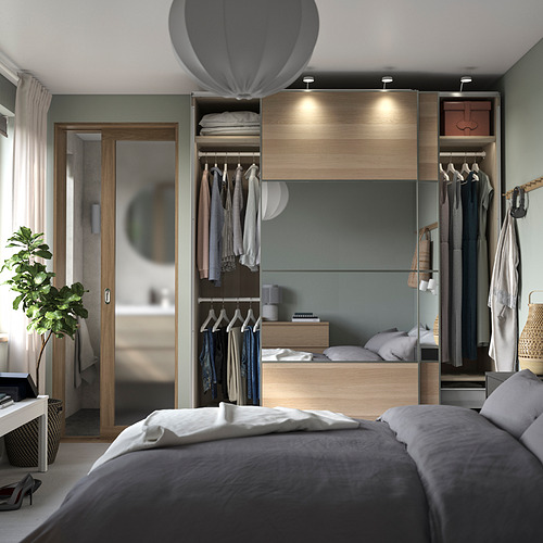 Dormitorio con ropa de cama gris, armario de madera, perchas y una planta.