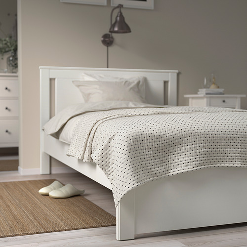 Dormitorio blanco minimalista con colcha JAKOBSLILJA en blanco roto, zapatillas, tocador, lámpara de pared.