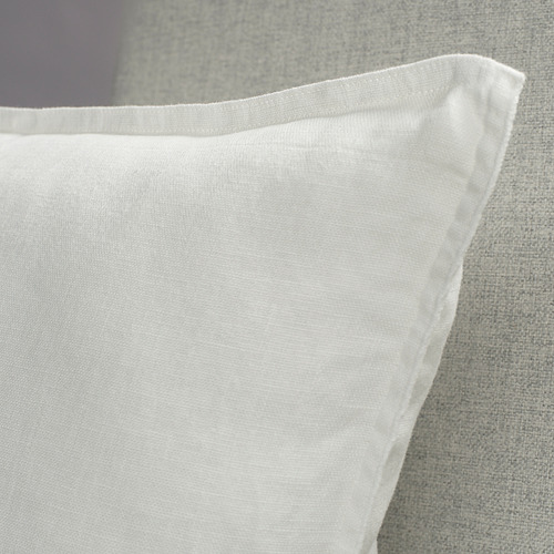 Primer plano de una funda de cojín de lino blanco sobre una superficie gris, mostrando su material suave y texturizado y sus costuras limpias.