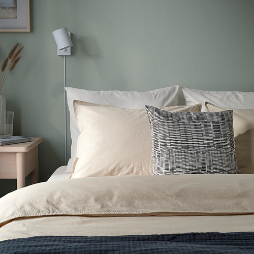Cama con cojín gris JORDKASTANJ, poliéster reciclado, entre almohadas blancas.