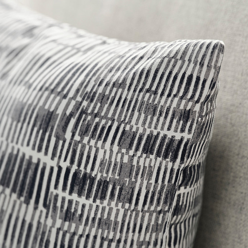 Primer plano de una almohada suave y estampada sobre una cama. Diseño geométrico en gris y blanco sobre tejido texturizado.