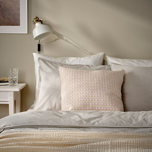 Una almohada MOROTSMOTT sobre una cama. La almohada es de color rosa claro con un patrón tejido. Es más pequeño que la cama y está rodeado de almohadas blancas más grandes.