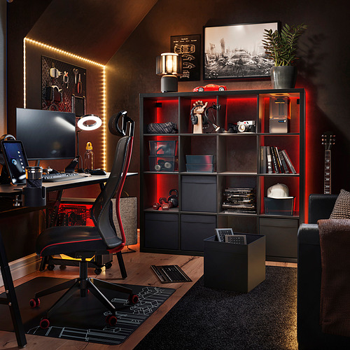 Moderna oficina en casa con estanterías negras KALLAX, luces rojas, escritorio para computadora, silla, guitarra y decoración.