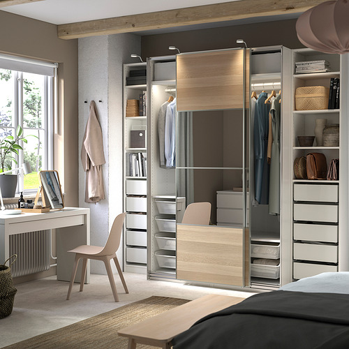 Un dormitorio moderno, un sistema de armarios PAX de madera clara y gris, con puertas correderas y estantes incorporados que sostienen ropa y artículos de decoración.