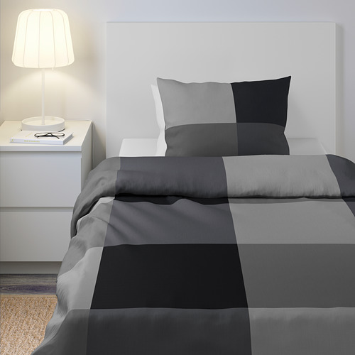 BRUNKRISSLA edredón y almohada de rayas grises, cama ordenada, pared, lámpara.