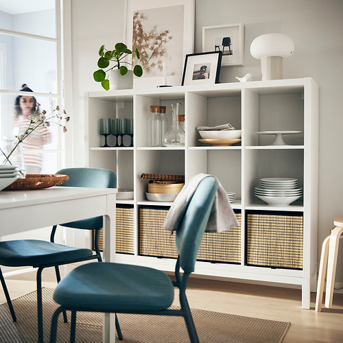 Comedor moderno con estanterías KALLAX blancas, sillas azules y elementos decorativos.