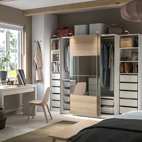 Dormitorio moderno con armario PAX de madera clara, con correderas con espejos, estantes y cajones. Escritorio, silla y alfombra completan el espacio organizado.