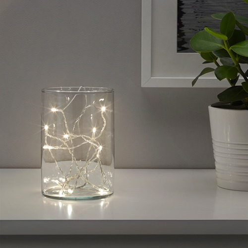 Jarrón transparente con cálidas luces led, planta al lado, decoración acogedora.