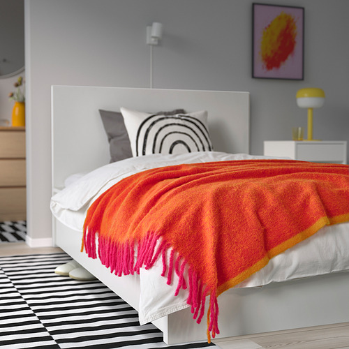 Manta KLIPPOXEL de color rosa brillante y naranja sobre una cama blanca, más grande que las almohadas, que agrega una calidez suave y esponjosa a la decoración acogedora.