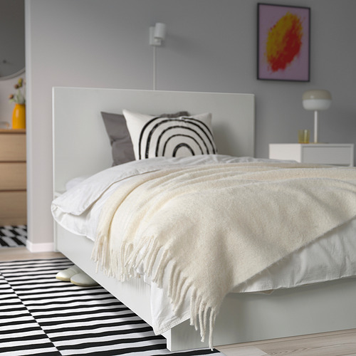 Acogedor dormitorio con manta blanca, almohada arcoíris, cama grande, alfombra de rayas. Suave, respetuoso con el medio ambiente.
