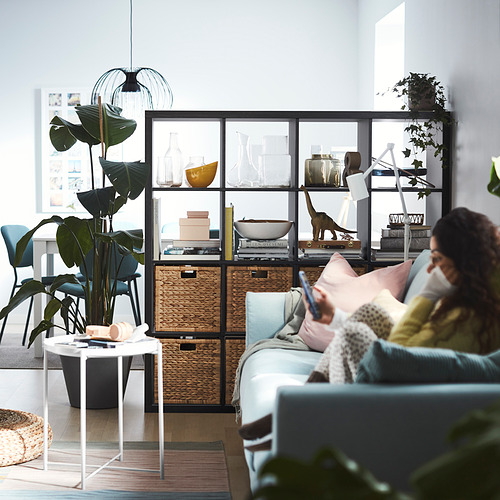 Sala de estar moderna con estante KALLAX azul, plantas y una persona en un sofá azul claro.
