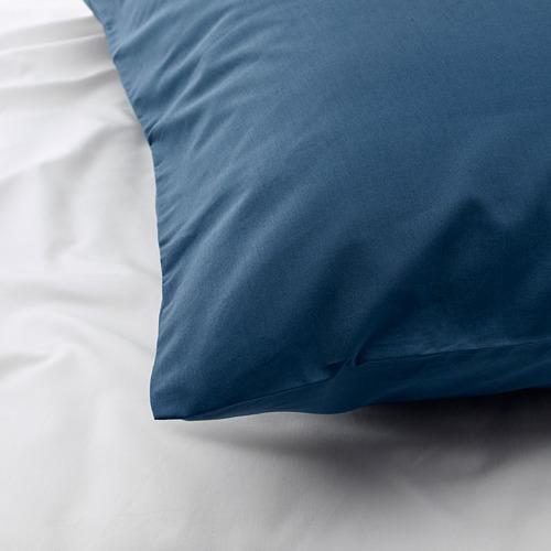 Funda de almohada azul sobre ropa de cama blanca. La tela suave y de alto número de hilos parece nítida y lisa.