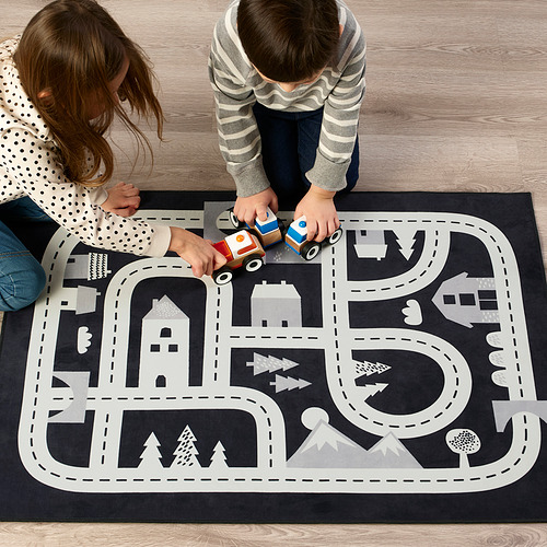 Los niños juegan con coches de juguete en una alfombra de juguete con carreteras y edificios, estimulando la imaginación y las habilidades sociales.
