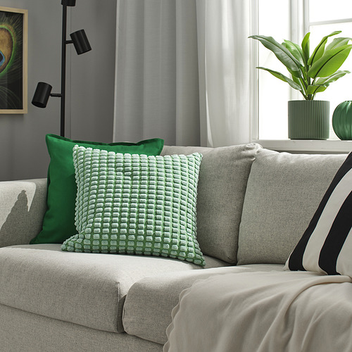 SVARTPOPPEL Funda de cojín verde claro sobre sofá gris, de textura suave, 16 cuadrados, con decoración vegetal moderna.