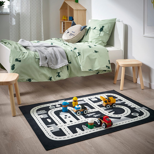 Habitación infantil con alfombra de juego MARKKRYPARE negra y gris con vehículos de juguete. La alfombra cabe debajo de una cama pequeña, taburetes de madera cerca.