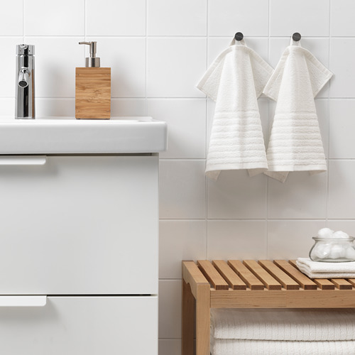 Baño moderno con toallas VÅGSJÖN, banco de madera y dispensador de jabón en un lavabo blanco.