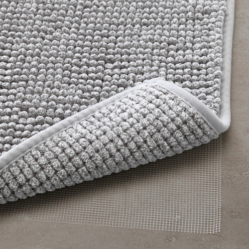 Primer plano de una alfombra de baño gris suave y texturizada con una parte inferior de malla antideslizante, lo que garantiza la seguridad y el secado rápido.