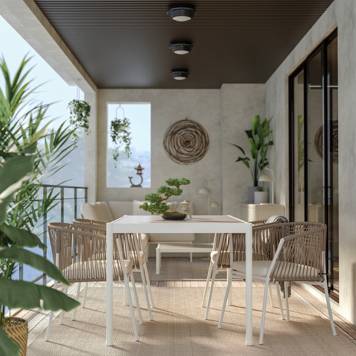 Modern outdoor dining set with white metal table and woven chairs on a patio with concrete walls and hanging plants.