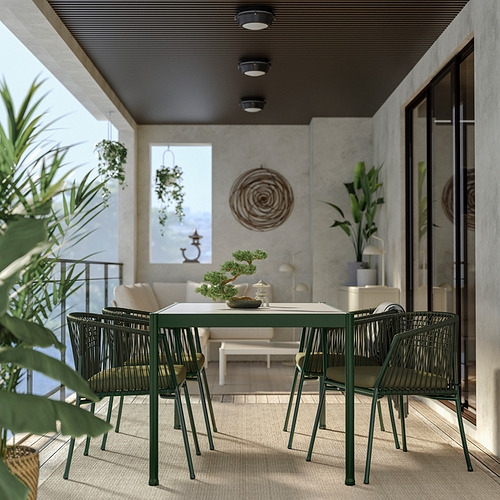 Moderno juego de comedor al aire libre: mesa rectangular de metal verde con sillas tejidas, rodeada de plantas en un balcón.