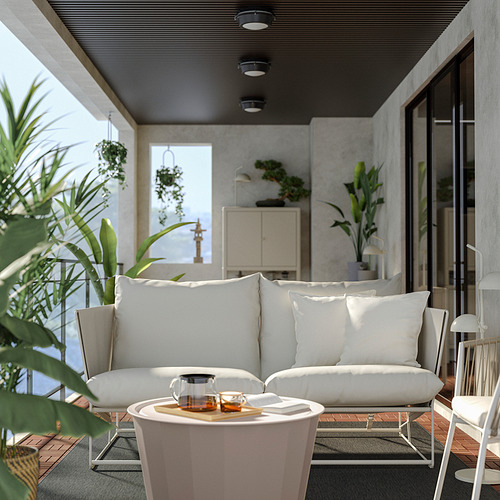 Moderno patio blanco con sofá HAVSTEN, cojines, juego de té de cristal, rodeado de plantas, decoración elegante.
