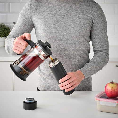 Vertiendo café en una taza de viaje negra en la encimera de la cocina.