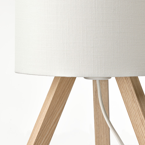 Una lámpara elegante y moderna con pantalla de tela blanca y patas de trípode de madera de fresno.