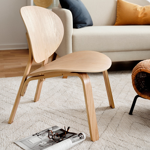 Silla minimalista de madera clara cerca de sofá crema, con alfombra beige y revista.