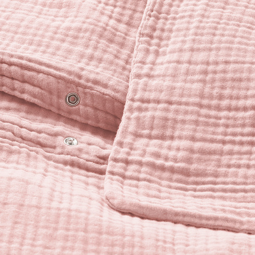 Primer plano de la funda nórdica de color rosa suave con cierre metálico de botón a presión en la parte inferior, con textura de muselina ondulada.