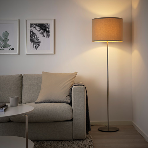 Moderno salón con lámpara de pie negra SKAFTET junto a un sofá beige, que proporciona mucha luz.
