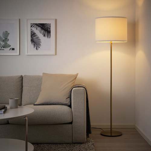 Salón moderno con lámpara de pie SKAFTET, pantalla blanca. Sofá gris, almohadas, decoraciones cerca de la pared.