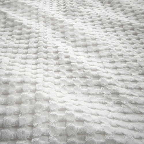 Primer plano de una colcha de algodón blanco con tejido de gofre, que muestra su naturaleza texturizada y reversible.