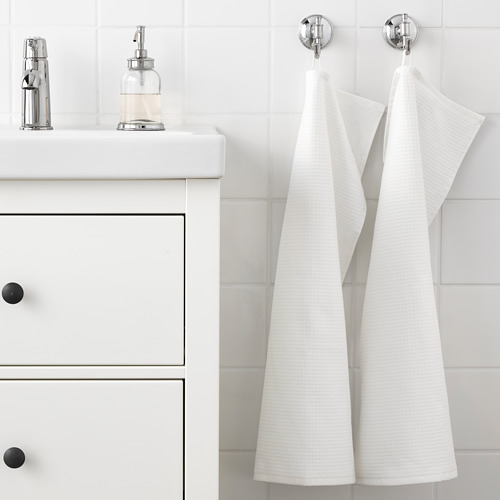 Baño blanco con dos toallas colgadas, una de rizo de un lado, otra de gofre, en ganchos junto a un lavabo con dispensador de jabón.