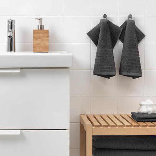 Baño moderno con lavabo blanco, grifo cromado, toallas VÅGSJÖN gris oscuro, dispensador de jabón de madera y estante de listones.