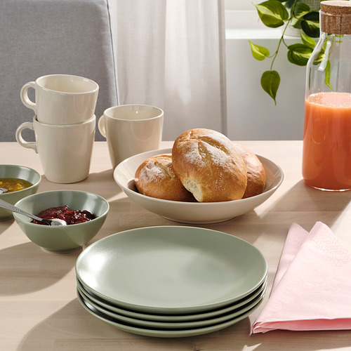 Mesa con platos de color verde claro, cuencos beige, tazas blancas, panecillos, mermeladas, zumo y servilletas rosas.