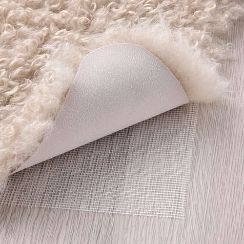 Alfombra esponjosa de color crema, respaldada con tela beige y malla antideslizante, perfecta para brindar calidez y comodidad.
