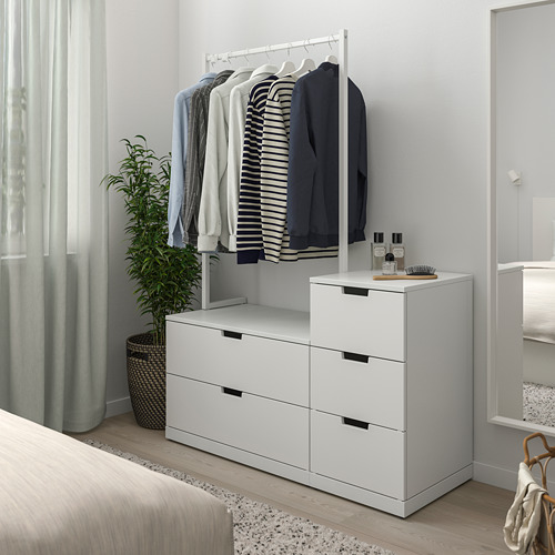 Cómoda NORDLI blanca moderna en el dormitorio junto a la cama. Barra de ropa arriba, planta al lado.