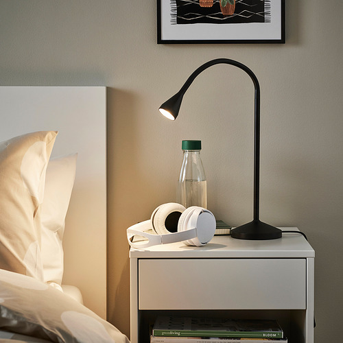 Dormitorio moderno con lámpara NÄVLINGE en cajón. Cuello flexible que dirige la luz. Cerca: auriculares, botella de agua, cama, obras de arte. El diseño elegante ahorra espacio.